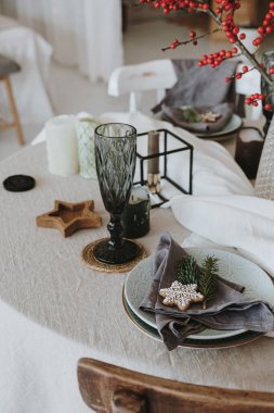 Zarif estetik Noel yemeği konsepti. Gri keten masa örtüsü, kırmızı böğürtlen buketi, zencefilli kurabiye, bardak, tabak. Noel kutlaması akşamı