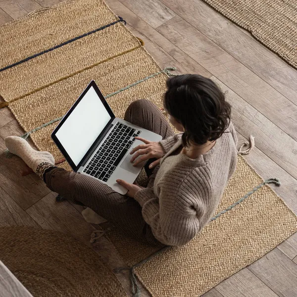 Top view of woman working on laptop computer sitting on wooden floor with carpet. Cozy comfortable home living room interior design. Blogger, freelancer work at home. Aesthetic view from above