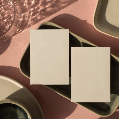 Tozlu pembe arka planda fotokopi alanı olan boş bir kağıt kağıdı. Estetik bohem iş modeli. Seramik tabaklar ve parlak güneş ışığı gölgeli cam.