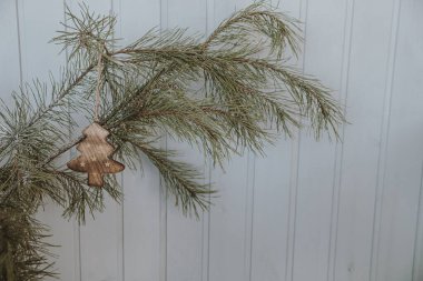 Beyaz ahşap duvarın önünde Noel oyuncağıyla süslenmiş köknar iğneleri. Minimalist Noel, Yılbaşı tatili geçmişi
