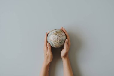 Kadının elleri mavi arka planda küçük bir küre tutuyor. Dünya, Dünya modeli ellerinde. Dünya 'yı ve çevreyi kurtar. Düz yatış, üst görünüm