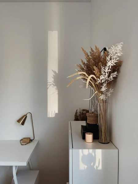 Aesthetic minimal office workspace interior design. Pampas grass floral bouquet on white table against white wall. Work at home business concept