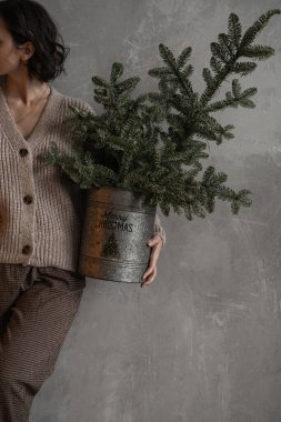 Genç ve güzel bir kadın elinde Noel ağacı dallarıyla el kovası tutuyor. Minimum moda festivali Noel ve Yeni Yıl kutlamaları konsepti.