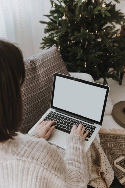 Kadın boş ekranlı dizüstü bilgisayarda çalışıyor. Evde çalış. Noel için dekore edilmiş modern oturma odası, Noel ağacı ile yeni yıl kutlaması. Kopyalama alanı şablonu