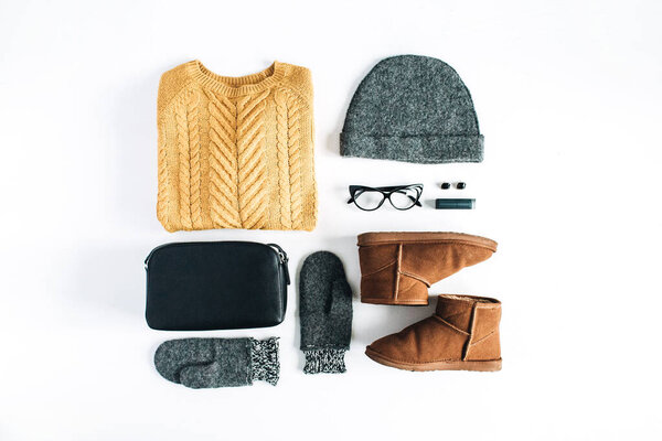 Flat lay setting of warm winter clothes and accessories. Women's fashion arrangement of woolen and knitted clothes: sweater, mittens, hat, boots on white background