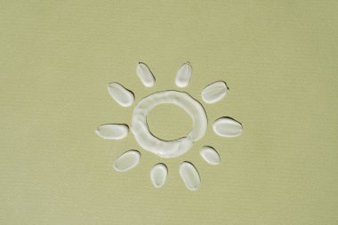 Tarafsız yeşil arka planda kozmetik krem lekesinden oluşan komik güneşi kapat. Minimalist güzellik markası, ticari ürün konsepti. Düz yatış, üst görünüm