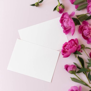 Blank paper invitation cards. Pink peony flowers bouquet on neutral pastel elegant pink background. Flat lay, top view minimal floral composition