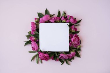 Zarif pembe şakayık çiçeklerinden yapılmış çelenk. Pastel pembe arka planda boş fotokopi kağıdı var. Düz yatak, üst görünüm markası, blog, web sitesi, sosyal medya şablonu