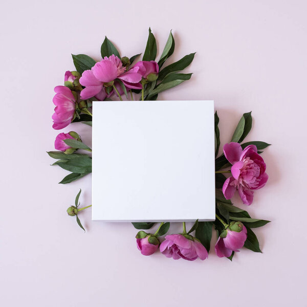 Wreath made of elegant pink peonies flowers with blank mockup copy space paper sheet on pastel pink background. Flat lay, top view brand, blog, website, social media template