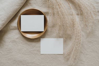 Fotokopi alanı olan boş kâğıt kartlar, tarafsız bej keten battaniyede kurutulmuş otlar. Üst görünüm, düz uzanan minimalist estetik lüks bohem ticari markalaşma kavramı