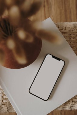 Flatlay cep telefonu, kurutulmuş çiçek buketi, rattan bankta albüm. Estetik zarif blog, çevrimiçi dükkan, mağaza, sosyal medya markalaşma şablonu