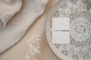 Damgalamak için boş fotokopi alanı olan kağıtlar. Davetiye şablonları, kurutulmuş çimen sapları, tarafsız bej arka planda süsleme tepsisi. Estetik lüks davetiye, marka kartları.