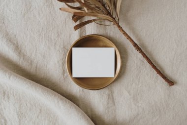 Estetik bir bohem düğün davetiyesi şablonu ve fotokopi alanı. Altın tepside kağıt kart, nötr bej keten battaniyede kurutulmuş protea çiçeği.