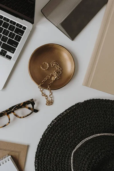 Flatlay laptop computer, fashionable women's bijouterie, jewelry, accessories on white table. Brass plate, glasses, straw hat, bracelet, ring. Aesthetic bohemian fashion online store, shop branding