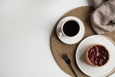 Tabakta tatlı turtasıyla kahvaltı, halıda bir fincan kahve. Kırmızı çiçek buketi ve keten battaniyeyle süslenmiş bir masa. Düz yatış, üst görünüm