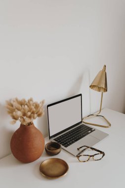 Masanın üzerinde beyaz duvara karşı kırtasiye malzemesi olan boş bir ekran olan dizüstü bilgisayar. Minimalist ev ofis çalışma alanı. Model şablonu