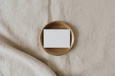Tarafsız bej keten battaniyenin üzerinde fotokopi alanı olan boş bir kağıt kart. Üst görünüm, düz uzanan minimalist estetik lüks bohem ticari markalaşma kavramı