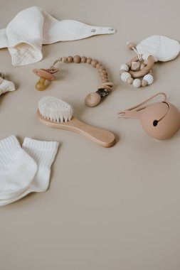 Tarafsız pastel bej arka planda zarif bebek aksesuarları ve oyuncak kolajı. Muslin önlüğü, fırça, emzik, çorap, emzik tutacağı
