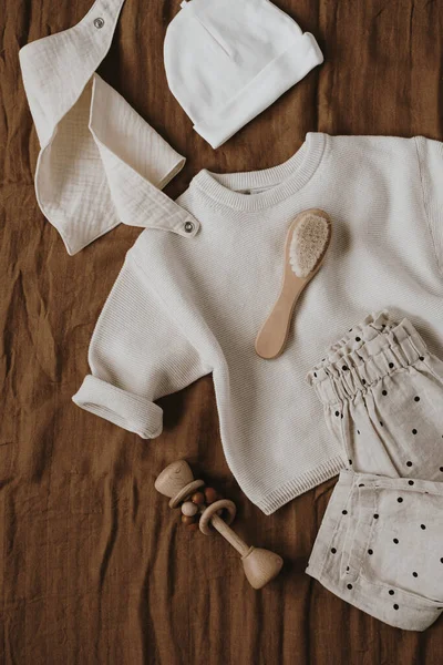 Flatlay aesthetic Scandinavian newborn baby clothes, accessories, toys on brown background. Trendy elegant luxury infant set. Top view