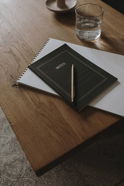 Aesthetic minimalist concept. Notebook, glass of water, stationery on wooden table background