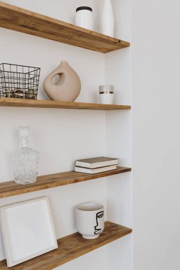 Beyaz duvarda dekore edilmiş raf. Estetik lüks minimalist ev dekorasyonu. Zarif İskandinav tarzı, hygge tarzı iç mekan. Resim çerçeveleri, parfüm, vazo, kitaplar, mum.