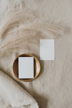 Fotokopi alanı olan boş kâğıt kartlar, tarafsız bej keten battaniyede kurutulmuş otlar. Üst görünüm, düz uzanan minimalist estetik lüks bohem ticari markalaşma kavramı