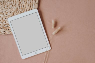 Düz tablet tablet, rattan peçete ve tavşan kuyruğu otları tarafsız pastel mercan arka planda. Estetik zarif blog, sosyal medya, web şablonu