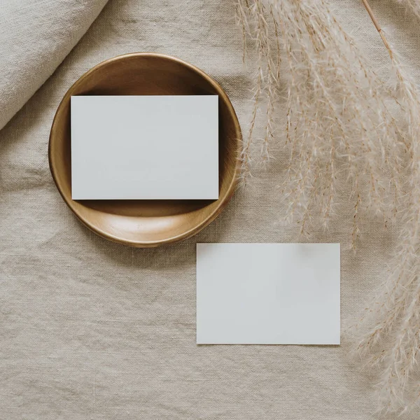 Fotokopi alanı olan boş kâğıt kartlar, tarafsız bej keten battaniyede kurutulmuş otlar. Üst görünüm, düz uzanan minimalist estetik lüks bohem ticari markalaşma kavramı