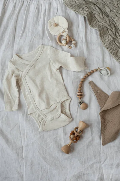 Beyaz pamuklu tulum, yeni doğmuş bebek oyuncakları, çarşaf battaniyesi. Bebek kıyafetleri ve aksesuarlar beyaz keten kumaş arka planda. Yeni doğmuş İskandinav kıyafetleri. Düz yatış, üst görünüm.