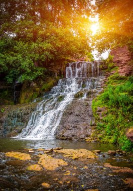 Dağlarda güneşli bir şelalenin fotoğrafı.