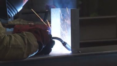 Fabrika işçisi metali kaynaklıyor. Adam kaynak yapıyor. Kaynak makinesi kullanarak argon veya elektrot ile kaynak yapmak. Metal yapılar üreten bir endüstriyel girişim. Kıvılcımlar ve parıltılar uçuşuyor.
