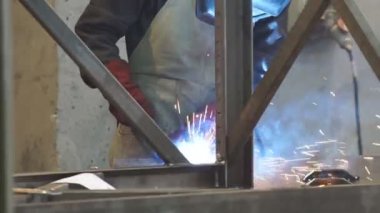 Fabrika işçisi metali kaynaklıyor. Adam kaynak yapıyor. Kaynak makinesi kullanarak argon veya elektrot ile kaynak yapmak. Metal yapılar üreten bir endüstriyel girişim. Kıvılcımlar ve parıltılar uçuşuyor.