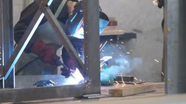 Fabrika işçisi metali kaynaklıyor. Adam kaynak yapıyor. Kaynak makinesi kullanarak argon veya elektrot ile kaynak yapmak. Metal yapılar üreten bir endüstriyel girişim. Kıvılcımlar ve parıltılar uçuşuyor.