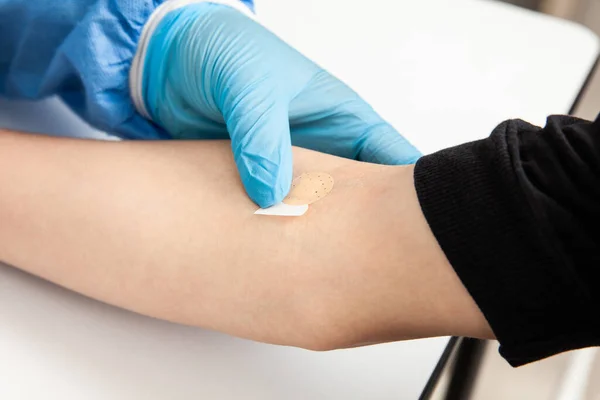 Nurse putting a Band-Aid on a patient\'s arm after taking a blood sample