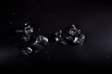 Siyah zemin üzerinde şeffaf buz parçaları. Arka planda su birikintilerindeki buz kütleleri. Yukarıdan buz görüntüsü.