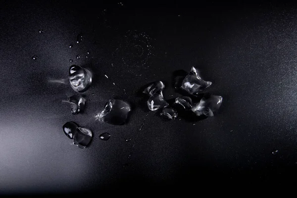 Siyah zemin üzerinde şeffaf buz parçaları. Arka planda su birikintilerindeki buz kütleleri. Yukarıdan buz görüntüsü.