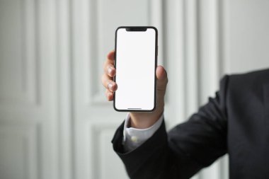 Ceketli ve takım elbiseli bir işadamı elinde bir akıllı telefon tutuyor. Elektronik aletler insanların elinde..