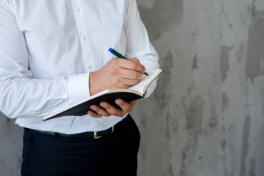 Kot pantolon ve beyaz gömlekli erkek danışman elinde açık siyah bir defter tutuyor. finansal planlama. Kavram - iş dünyasındaki geleneksel teknolojiler