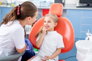 Pediatrik dişçi küçük bir kızla konuşur ve dişlerine nasıl bakacağını söyler. Güzel kız dişçinin ofisinde gülümsüyor. konsept bir çocuk tıbbi muayenesidir..