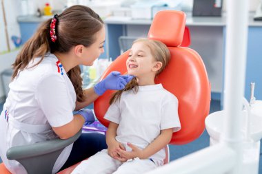 Pediatrik dişçi küçük bir kızla konuşur ve dişlerine nasıl bakacağını söyler. Güzel kız dişçinin ofisinde gülümsüyor. konsept bir çocuk tıbbi muayenesidir..