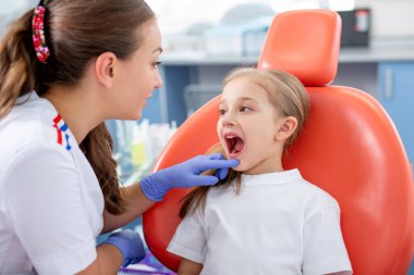 Pediatrik dişçi küçük bir kızla konuşur ve dişlerine nasıl bakacağını söyler. Güzel kız dişçinin ofisinde gülümsüyor. konsept bir çocuk tıbbi muayenesidir..