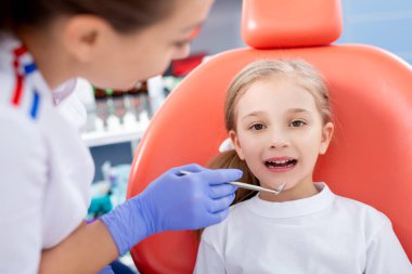 Pediatrik dişçi küçük bir kızın karnını kontrol ediyor. Güzel kız dişçinin ofisinde gülümsüyor. konsept bir çocuk tıbbi muayenesidir..