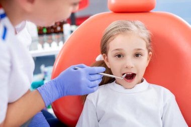 Pediatrik dişçi küçük bir kızın karnını kontrol ediyor. Güzel kız dişçinin ofisinde gülümsüyor. konsept bir çocuk tıbbi muayenesidir..