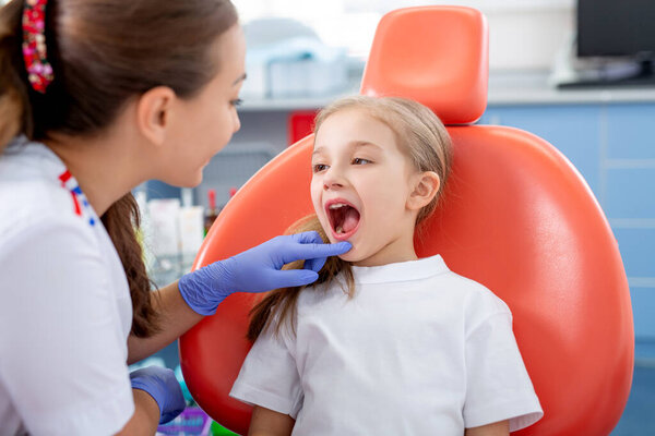 pediatric dentist talks to a little girl and tells her how to take care of her teeth. beautiful girl is smiling in the dentist's office. concept is a children's medical examination.