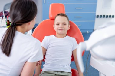 Dişi dişçi genç bir çocukla konuşur ve ona dişlerine nasıl bakacağını söyler. Yakışıklı çocuk dişçinin ofisinde gülümsüyor. konsept bir çocuk tıbbi muayenesidir..