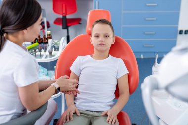 Dişi dişçi genç bir çocukla konuşur ve ona dişlerine nasıl bakacağını söyler. Yakışıklı çocuk dişçinin ofisinde gülümsüyor. konsept bir çocuk tıbbi muayenesidir..