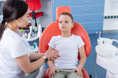 Dişi dişçi genç bir çocukla konuşur ve ona dişlerine nasıl bakacağını söyler. Yakışıklı çocuk dişçinin ofisinde gülümsüyor. konsept bir çocuk tıbbi muayenesidir..