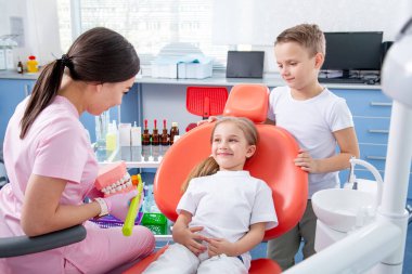 Pediatrik dişçi küçük bir kızın diş çürüğünü muayene ediyor. Oğlan küçük kıza doktordan korkmaması için yardım ediyor. konsept, çocuk dişlerinin sağlığıdır.