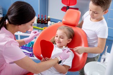 Pediatrik dişçi küçük bir kızın diş çürüğünü muayene ediyor. Oğlan küçük kıza doktordan korkmaması için yardım ediyor. konsept, çocuk dişlerinin sağlığıdır.