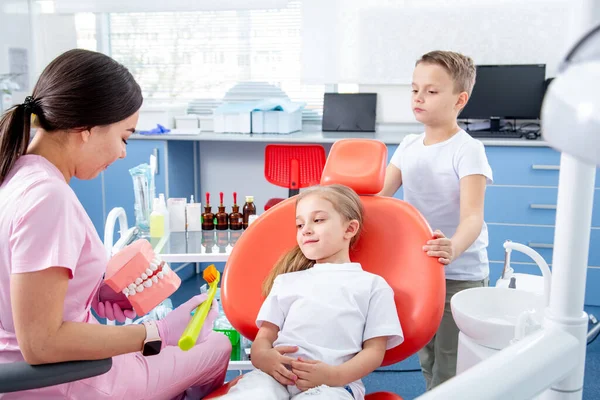 Pediatrik dişçi küçük bir kızın diş çürüğünü muayene ediyor. Oğlan küçük kıza doktordan korkmaması için yardım ediyor. konsept, çocuk dişlerinin sağlığıdır.